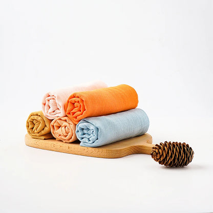Stack of folded towels on a wooden board with a pine cone on a white background