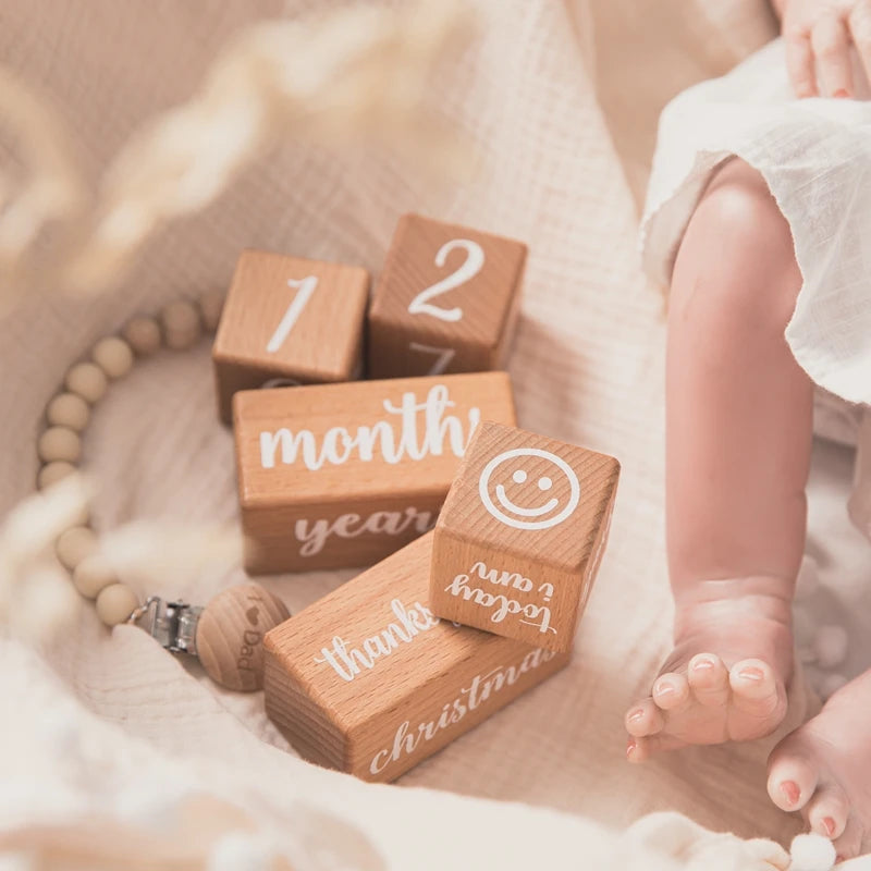 Wooden blocks with milestone text next to a baby's feet