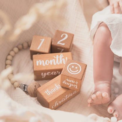 Wooden blocks with milestone text next to a baby's feet