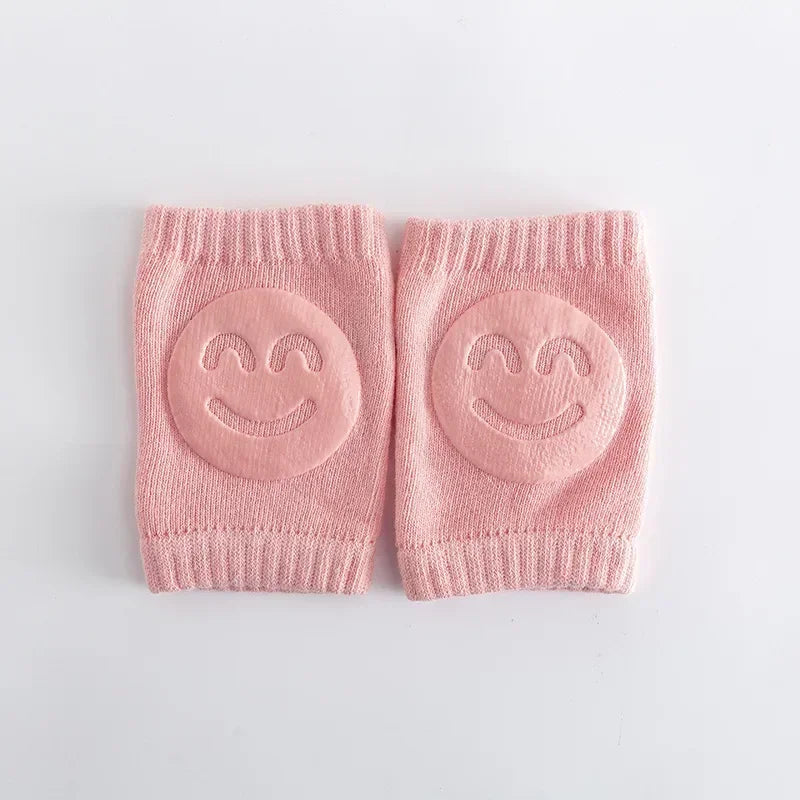 Pair of pink baby knee pads with smiley face designs on a light gray background