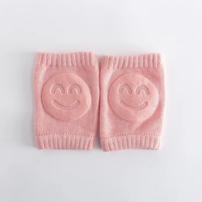 Pair of pink baby knee pads with smiley face designs on a light gray background