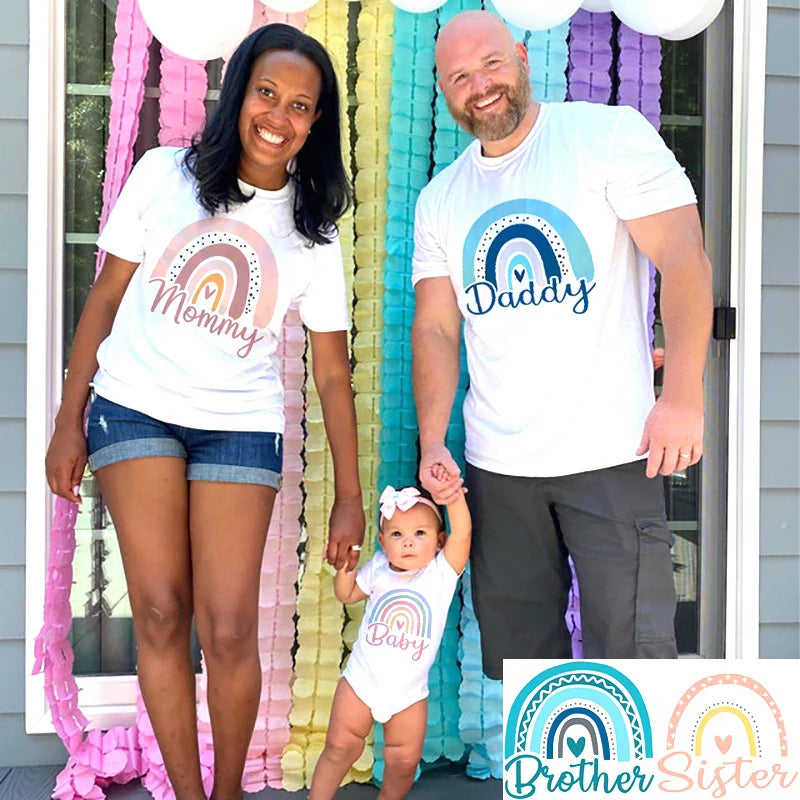 Family of three wearing matching shirts with rainbow designs and text in front of colorful decorations.