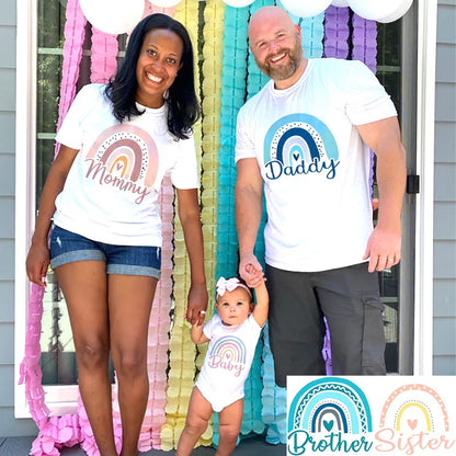 Family of three wearing matching shirts with rainbow designs and text in front of colorful decorations.