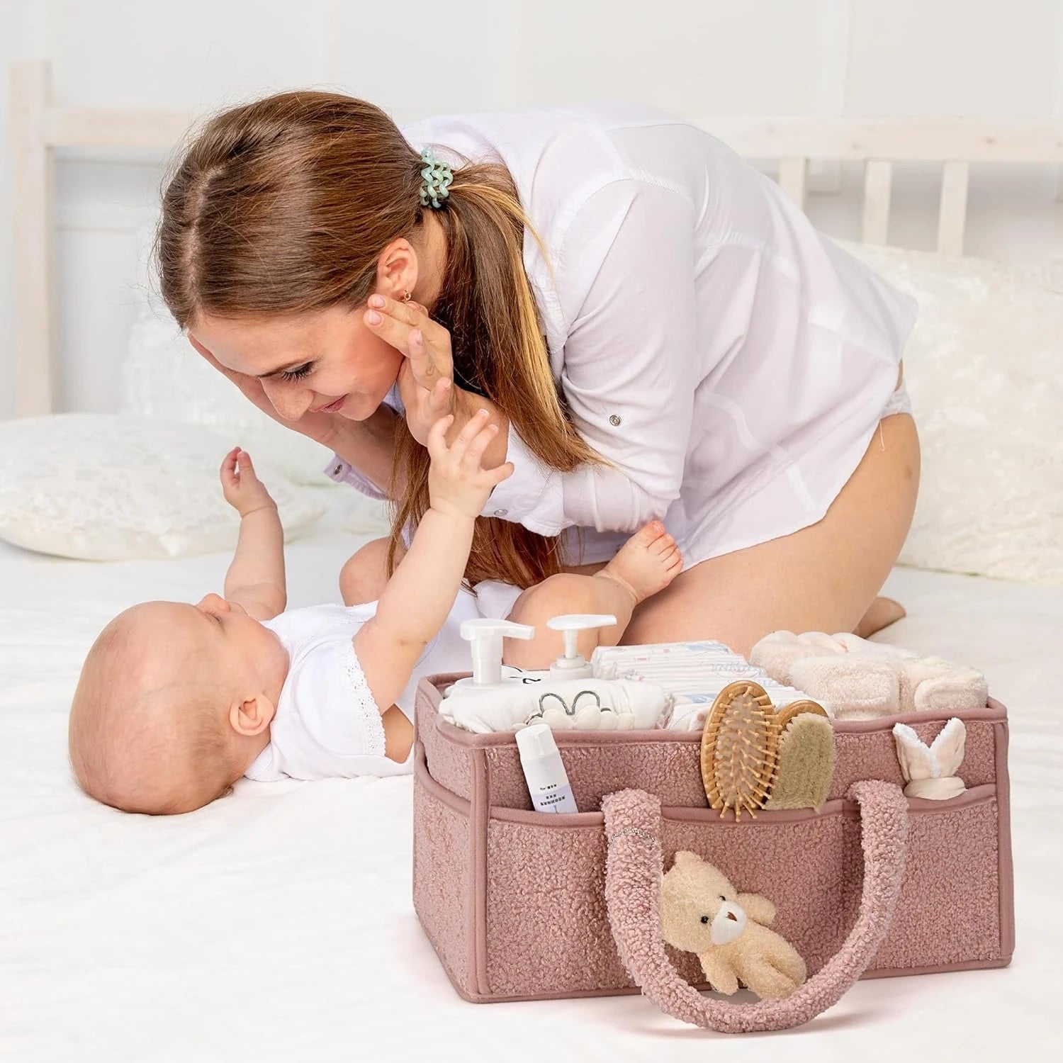 Woman playing with a baby on a bed next to a pink baby organizer.
