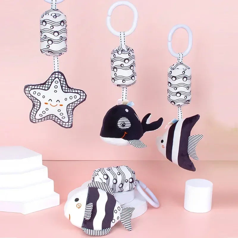 Set of black and white baby toys with star, whale, and fish designs on a pink background.
