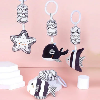 Set of black and white baby toys with star, whale, and fish designs on a pink background.