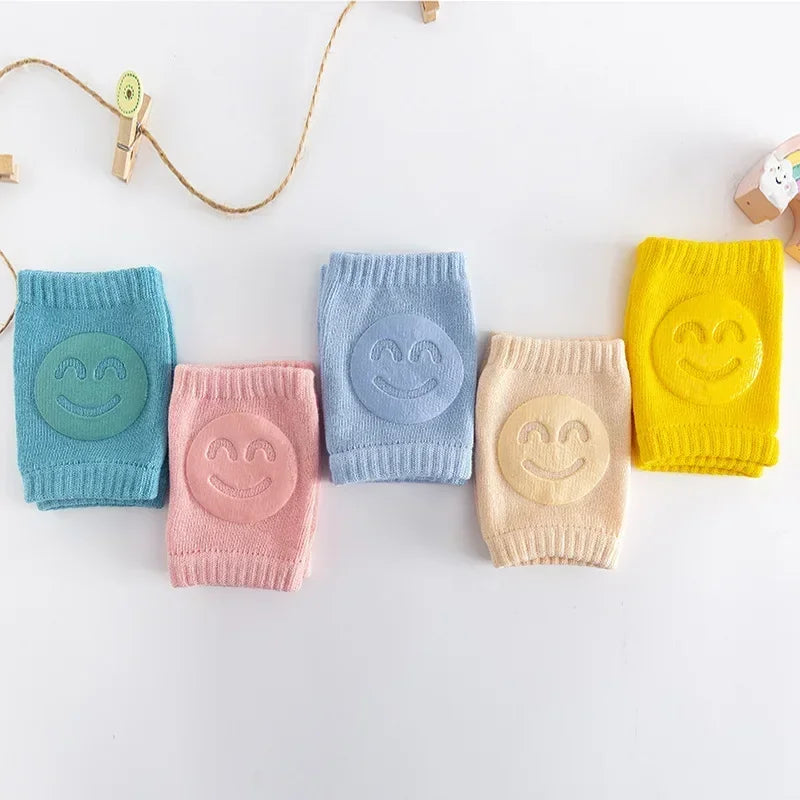 Five colorful baby knee pads with smiley face designs on a white background