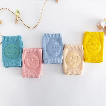 Five colorful baby knee pads with smiley face designs on a white background