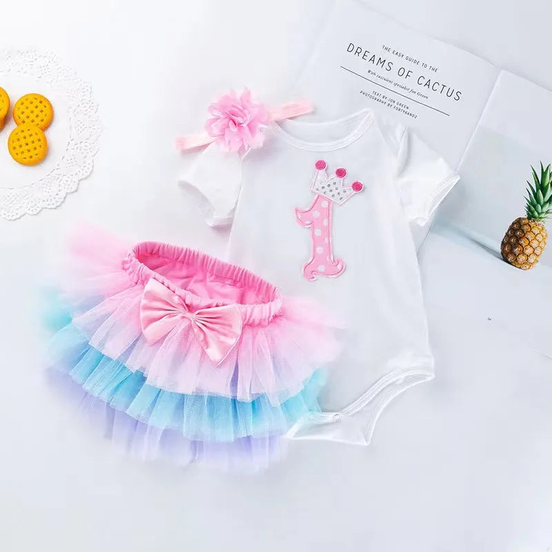 Baby outfit with white onesie, colorful tutu, and pink headband on a light background
