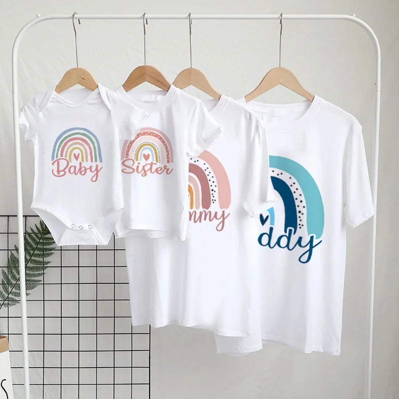Set of white t-shirts with rainbow designs and text on a rack against a neutral background