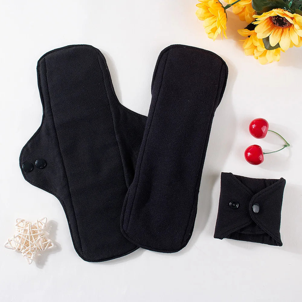 Two black reusable pads on a white surface with yellow flowers and red cherries.