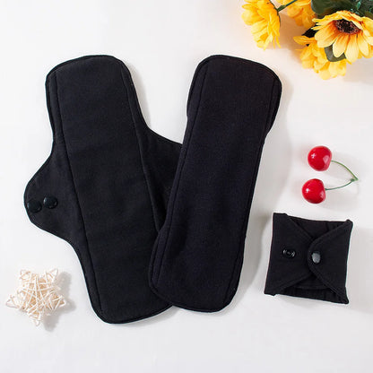 Two black reusable pads on a white surface with yellow flowers and red cherries.