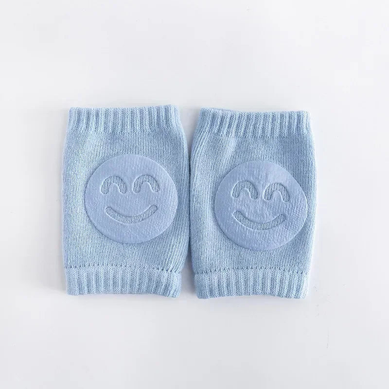 Pair of light blue baby knee pads with smiley face designs on a white background