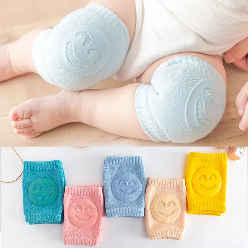 Baby wearing light blue knee pads with smiley face design, followed by a row of colorful knee pads on a white background.