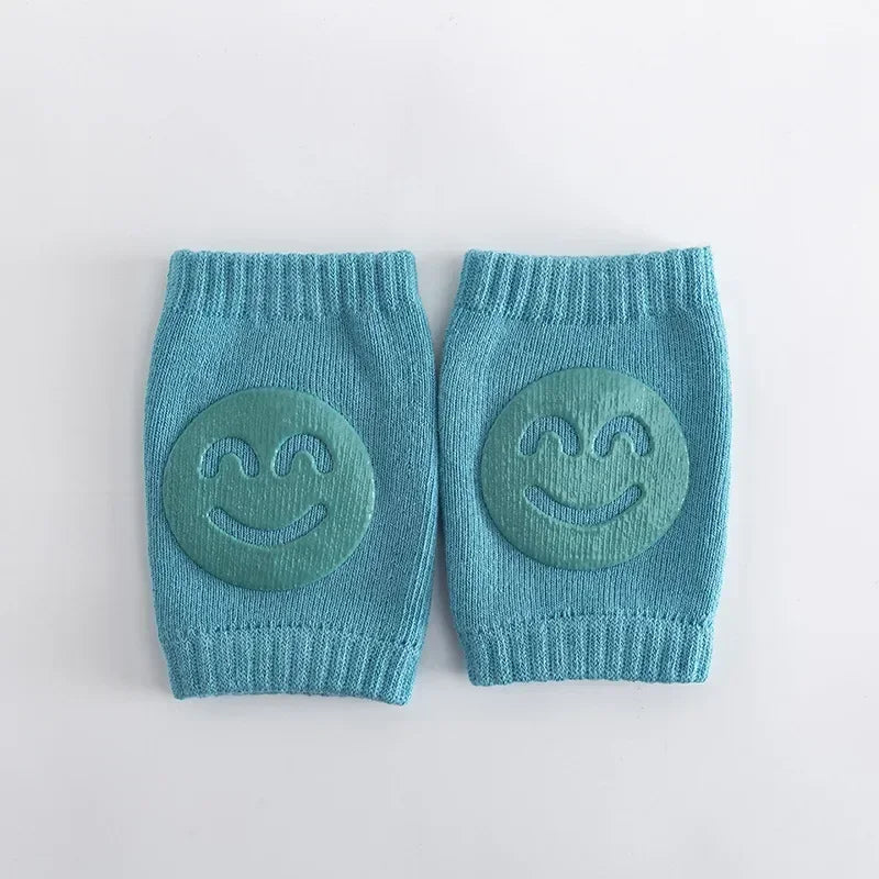 Pair of blue knitted baby knee pads with smiley face designs on a light gray background