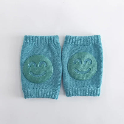 Pair of blue knitted baby knee pads with smiley face designs on a light gray background