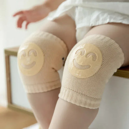 Baby wearing beige knee pads with smiley face designs on a light background