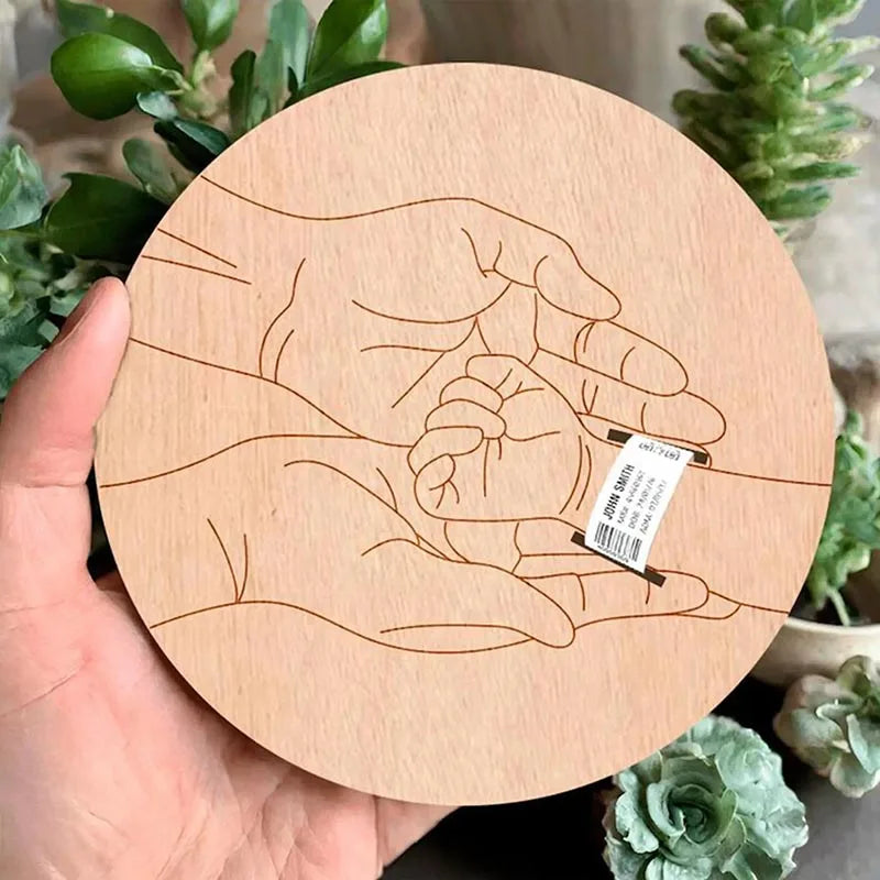 Wooden coaster with engraved design of hands holding a heart, held in front of green plants.