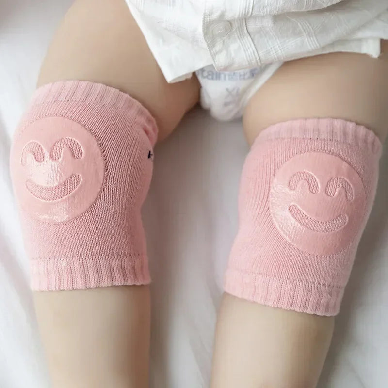 Pink knee pads with smiley face design on a baby's legs.