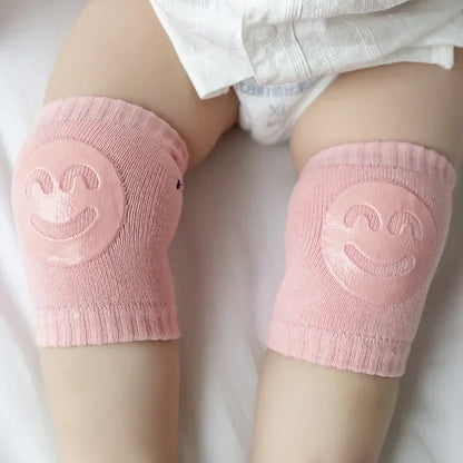 Pink knee pads with smiley face design on a baby's legs.