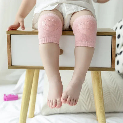 Child wearing pink knee pads with smiley face designs on a wooden stool.