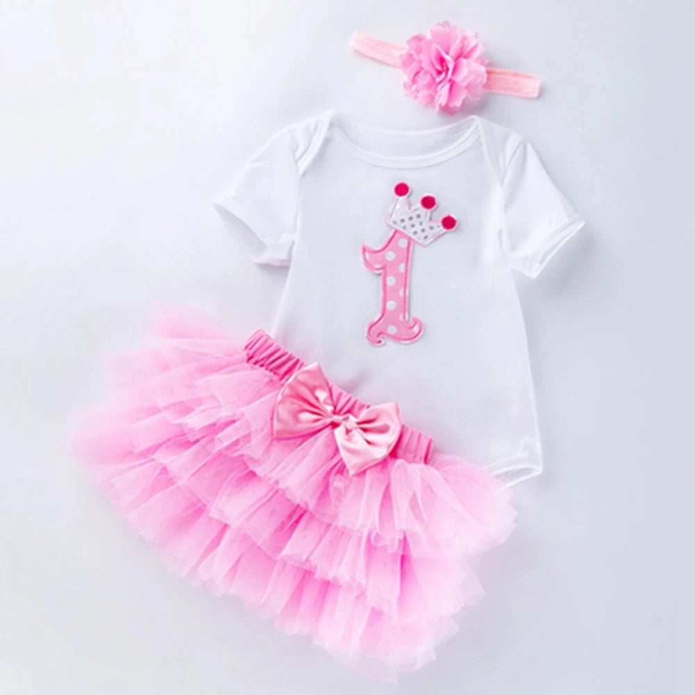Baby girl's first birthday outfit with pink tutu, number 1 shirt, and headband on a light gray background