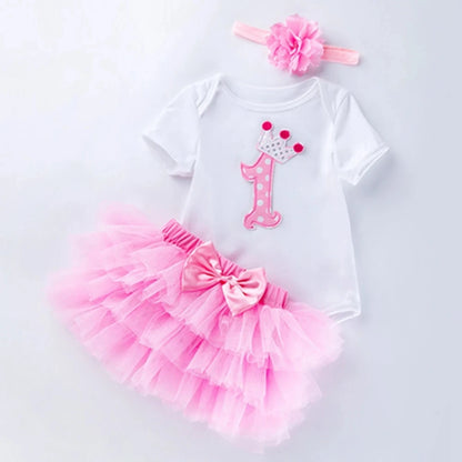 Baby girl's first birthday outfit with pink tutu, number 1 shirt, and headband on a light gray background