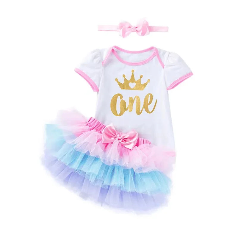 Baby girl's first birthday outfit with colorful skirt, white top with gold 'One' and pink headband on a white background.