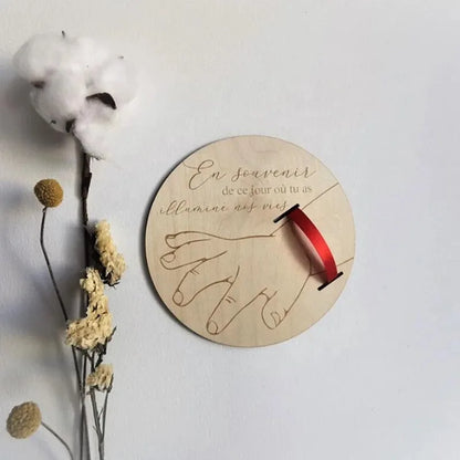 Decorative wall piece with hands holding a red ribbon and text on a light background