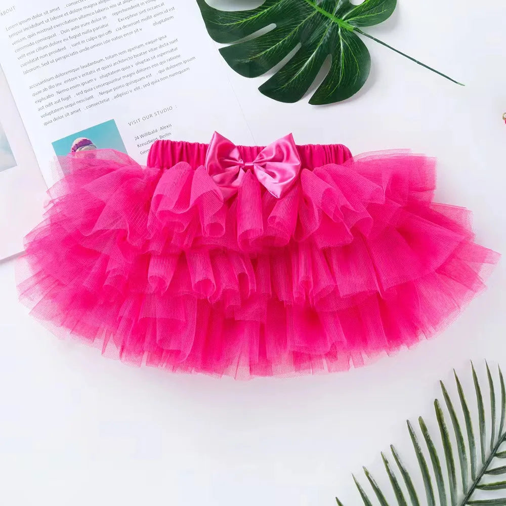 Pink tutu skirt with a bow on a white surface with green leaves.