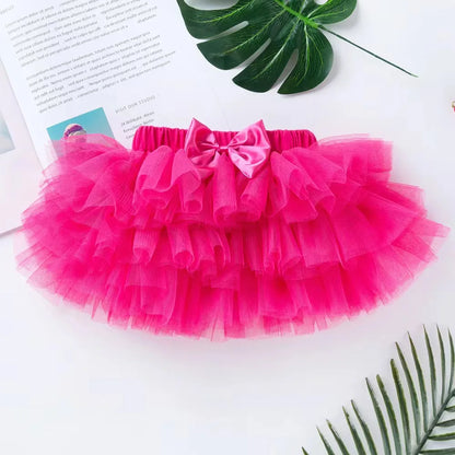 Pink tutu skirt with a bow on a white surface with green leaves.
