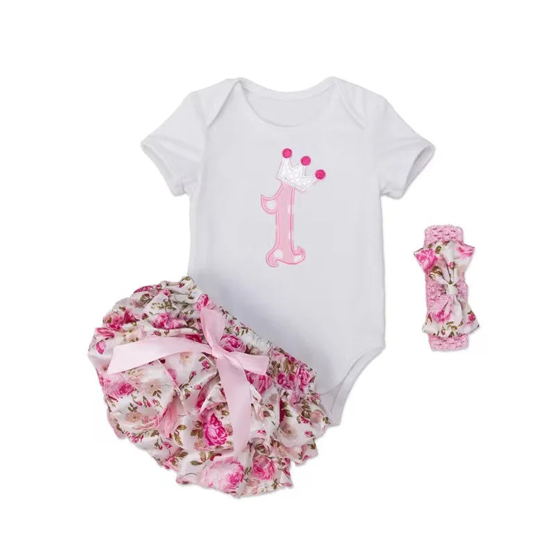 Baby girl's first birthday outfit with floral bloomers and pink number 1 onesie on a white background