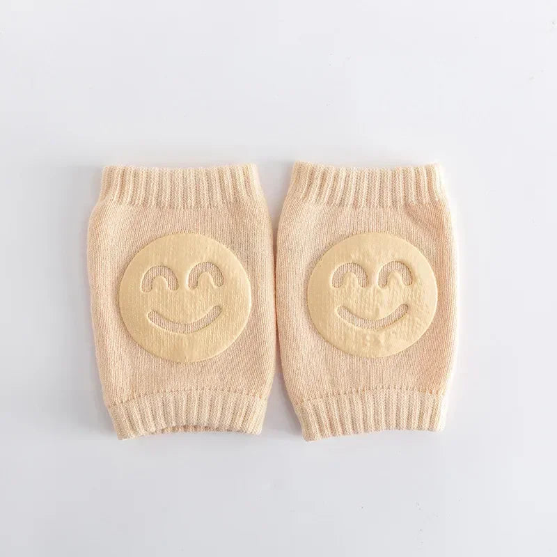 Pair of beige baby leg warmers with smiley face designs on a light gray background
