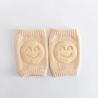 Pair of beige baby leg warmers with smiley face designs on a light gray background