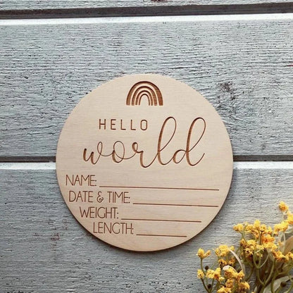 Round wooden plaque with engraved text 'Hello world' on a wooden surface with yellow flowers.