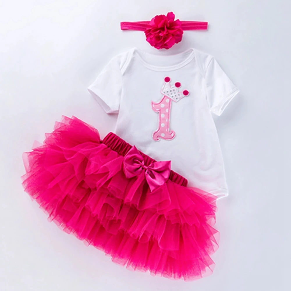 Baby girl's first birthday outfit with white top, pink tutu skirt, and headband on a white background